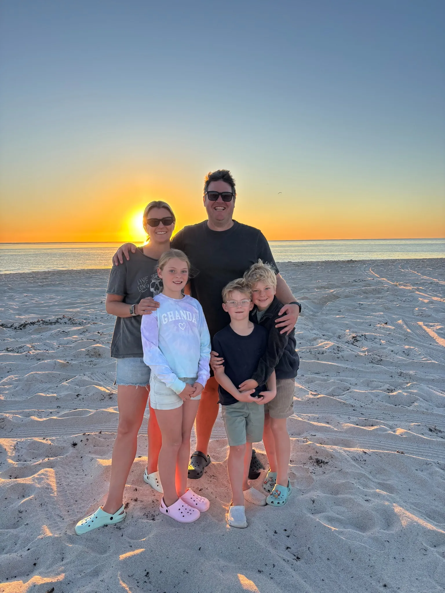 Josh and Christie, founders of South West Threads, with their three children on a beach at sunset